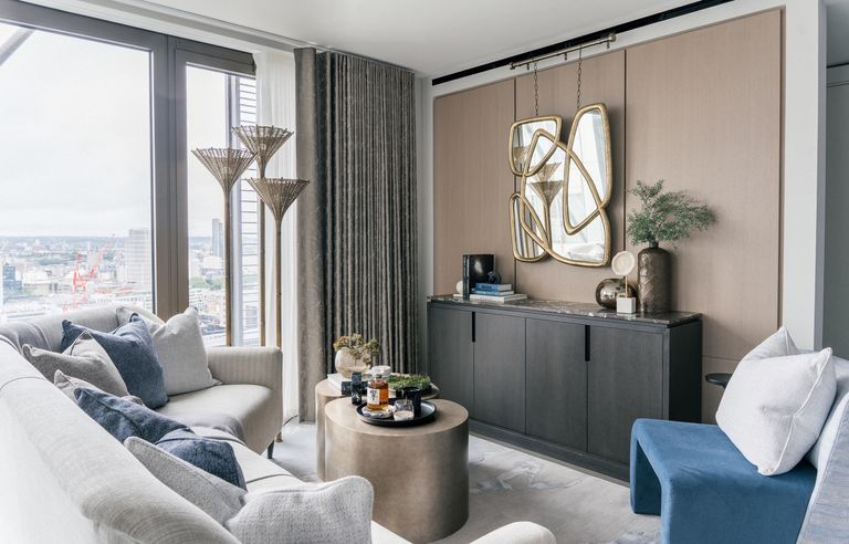 A statement mirror hanging in an apartment living room with brown walls and cream sofa overlooking a city
