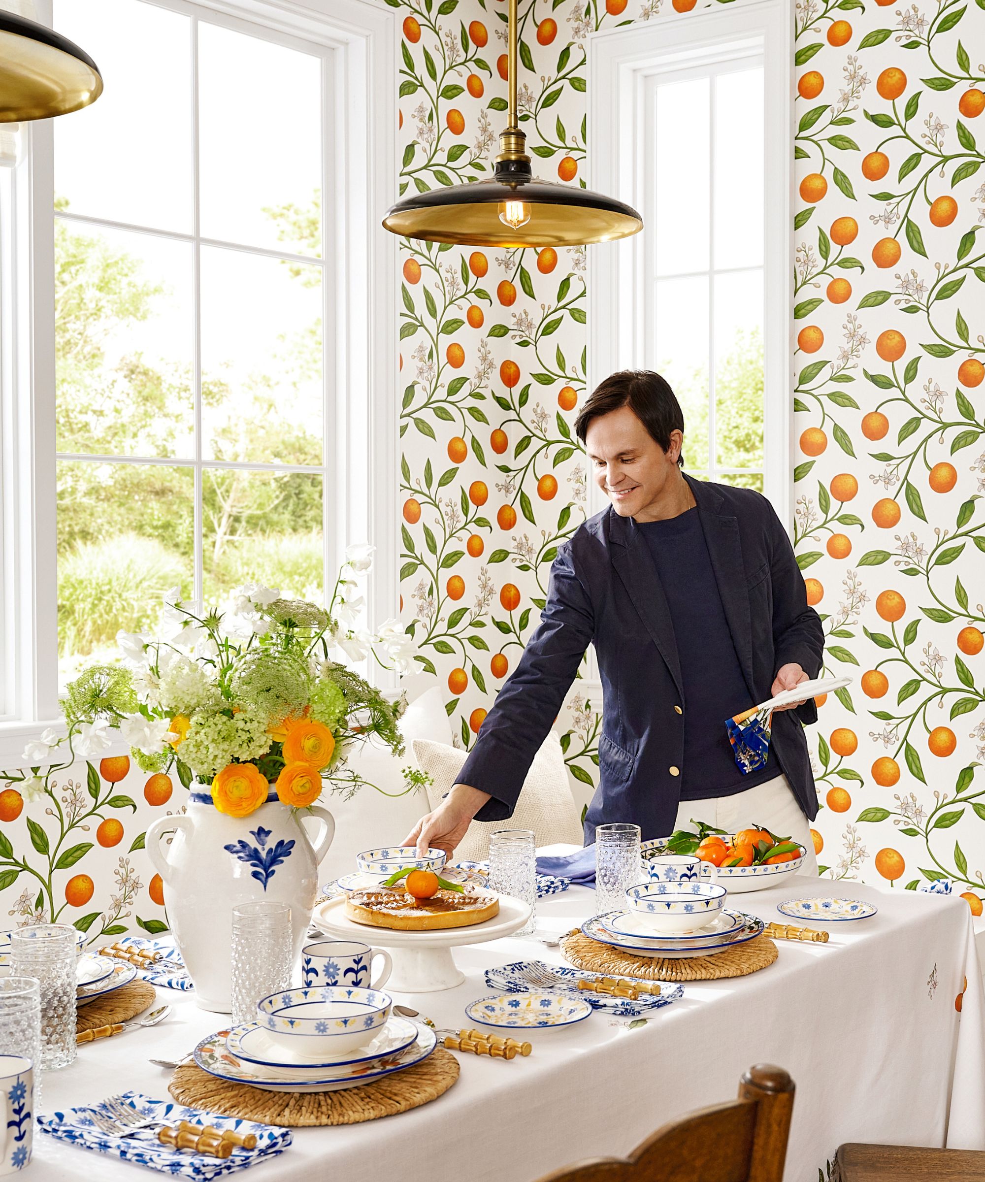 Mark D. Sikes for pottery barn collab photographed in a dining nook with citrus orange wallpaper and a blue and white styled tablescape with orange accents