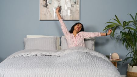 Tester Becky George wakes up smiling, her arms outstretched, after a great night's sleep on the Saatva Classic mattress