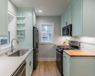 Light blue galley kitchen with open shelves for glassware and built-in microwave to save space