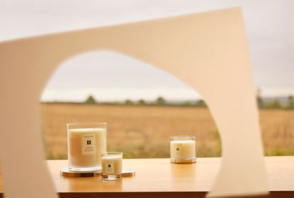 Jo Malone London scented candles on a table outdoors, seen through a cut-out