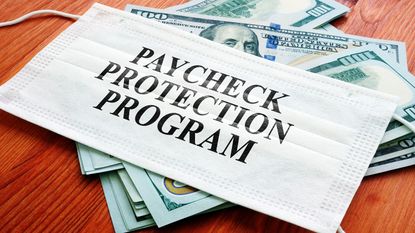 picture of mask with "paycheck protection program" written on it sitting on money