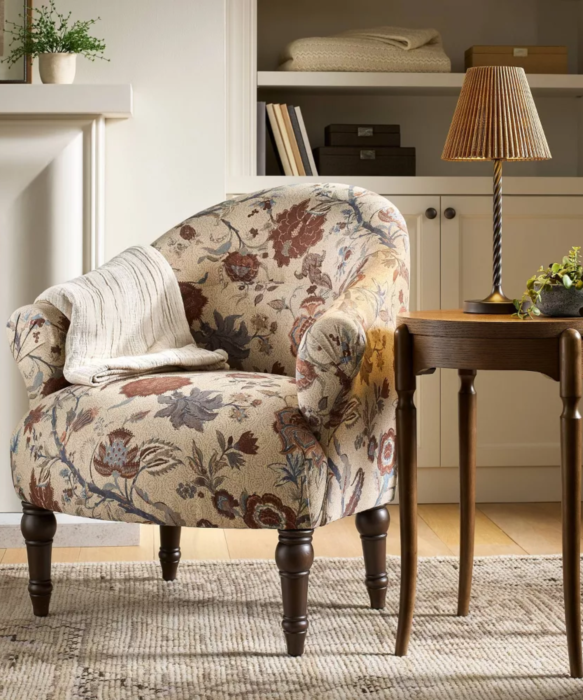 a floral chair with a blanket draped over the side, a side table, and a portable lamp