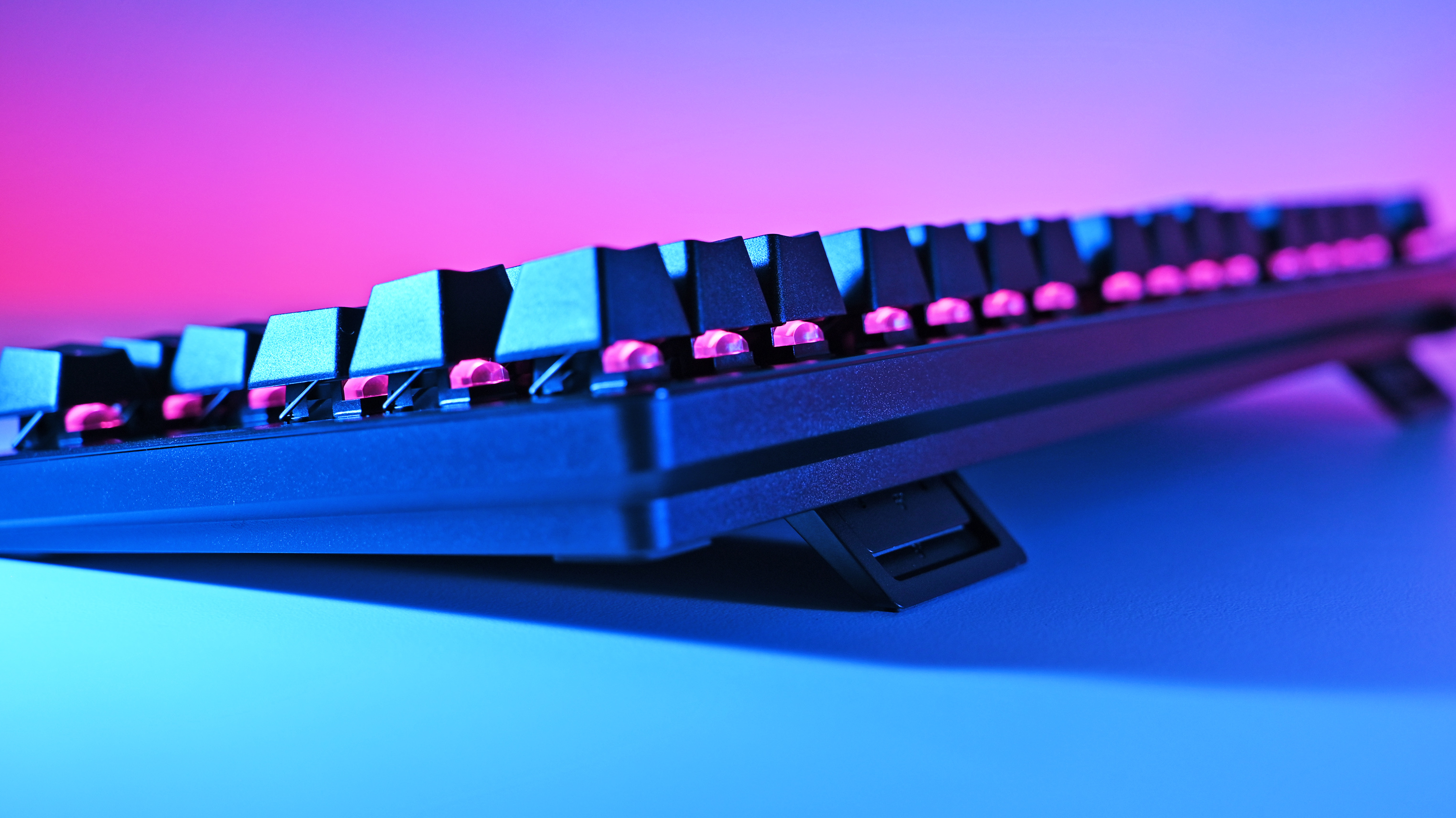 Close-up of Razer Huntsman V3 Pro TKL 8KHz keyboard with raised keys, illuminated by blue and pink lighting from below, creating a vibrant, futuristic atmosphere.