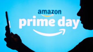 Amazon Prime Day logo in background with woman standing in the foregroud holding a phone