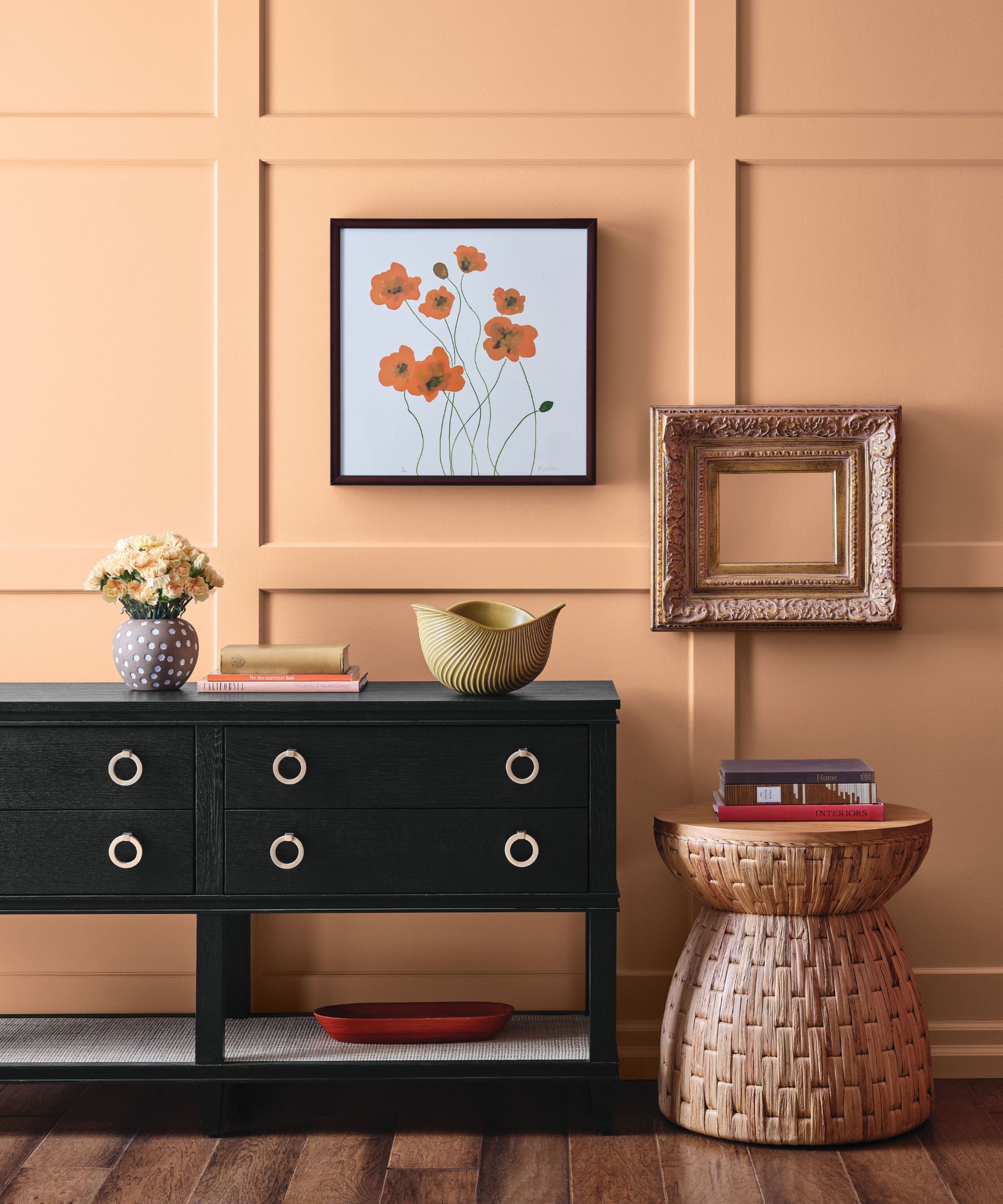 Entryway with orange walls, rattan stool, black console and art on walls
