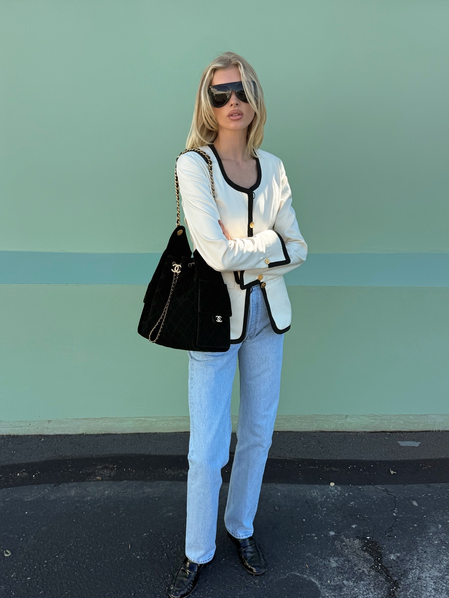 Elsa Hosk wears a white jacket with black trim over light-wash blue jeans with black loafers and a black Chanel shoulder bag.