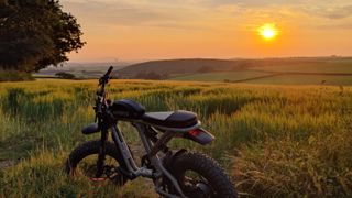 A Super73 e-bike in a field overlooking a hilly landscape and a sunset