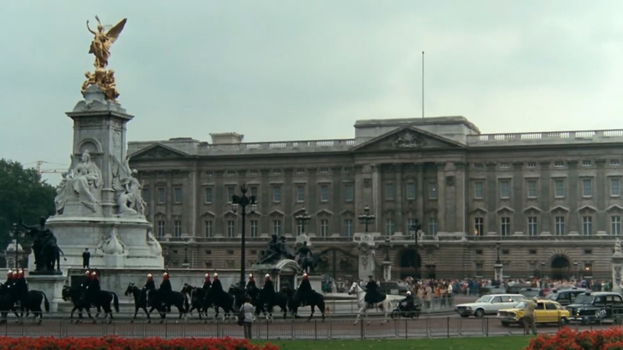 A yellow car driving in front of Buckingham Palace in National Lampoon's European Vacation