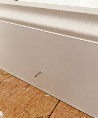 a nail sticking out the side of a piece of white skirting board
