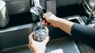 Woman's hands holding glass under a kitchen water tap