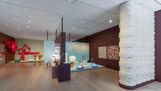 A design exhibition featuring furniture pieces, standing installations, wall art and clothing is on display in a gallery setting.