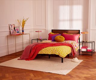 bedroom with richly toned wooden floor soft peach wall panelling and bed with brightly coloured fabrics