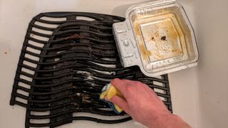 Cleaning barbecue grill grates using a soapy scouring pad in a sink