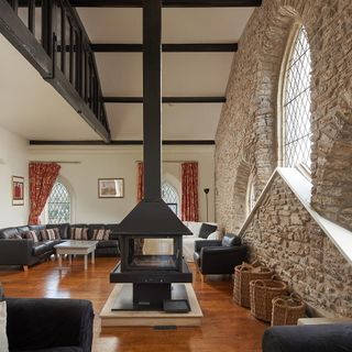 living area with central log-burning stove and vaulted ceiling and arched windows and wooden floor and stone expeosed wall