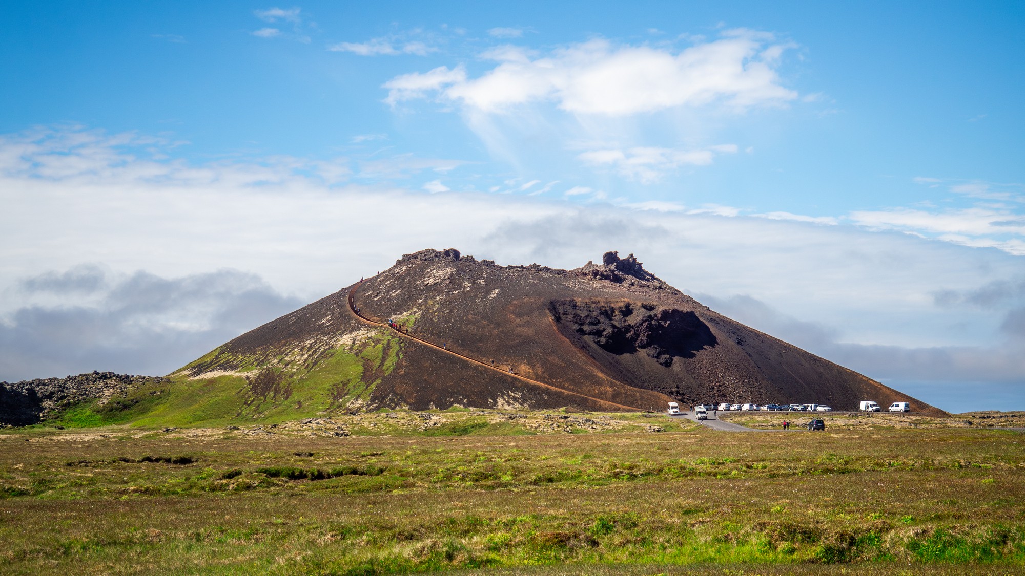 a tall brown mound in the background and in the foreground is a grassy landscape.