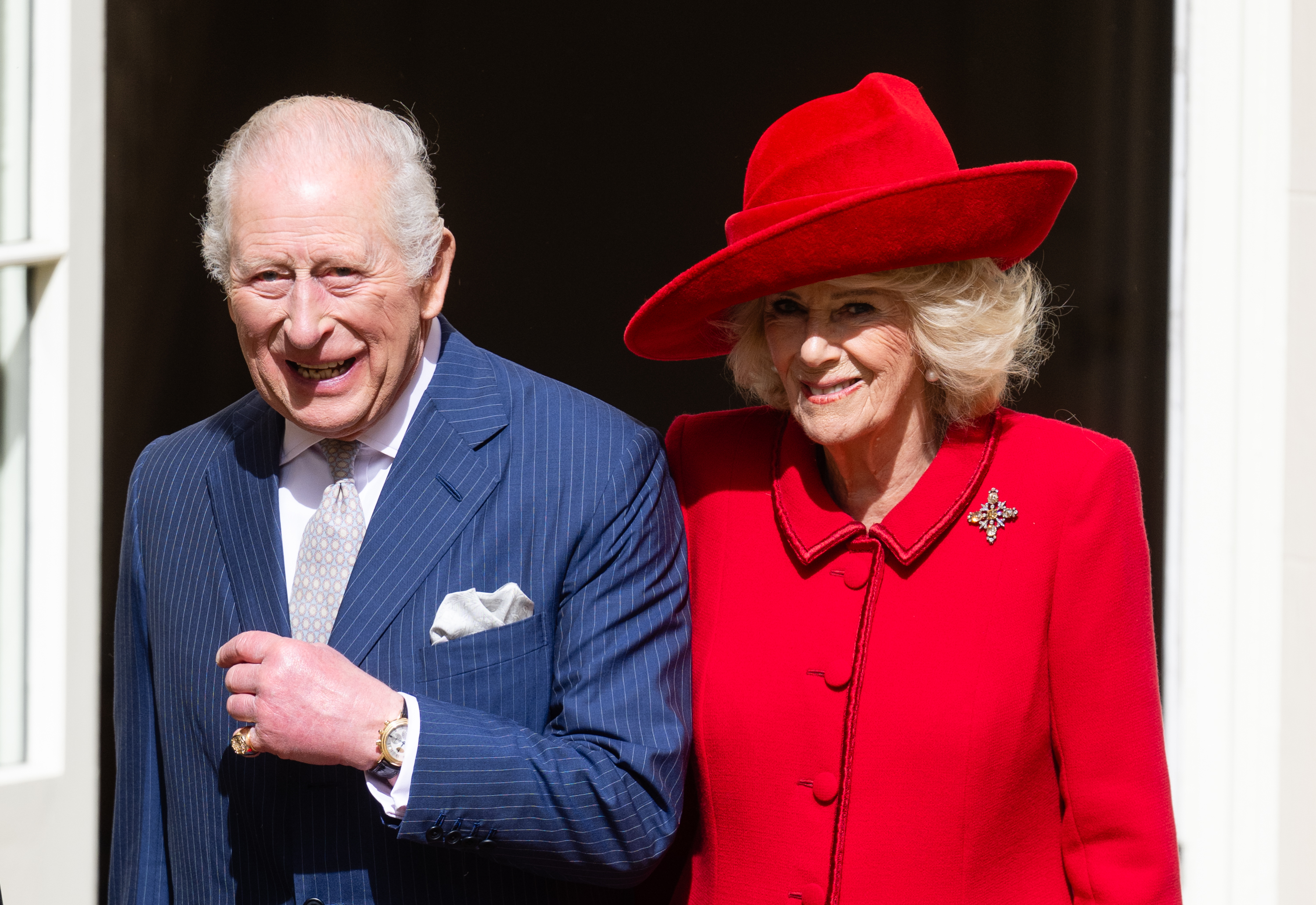 King Charles in a blue suit and Queen Camilla in a red coat and hat posing on Easter