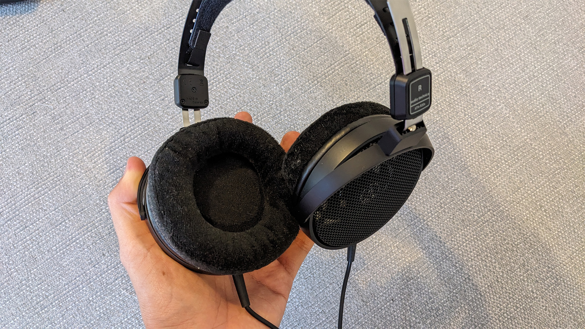 Audio-Technica ATH-R30x over-ear headphones held in hand over grey surface