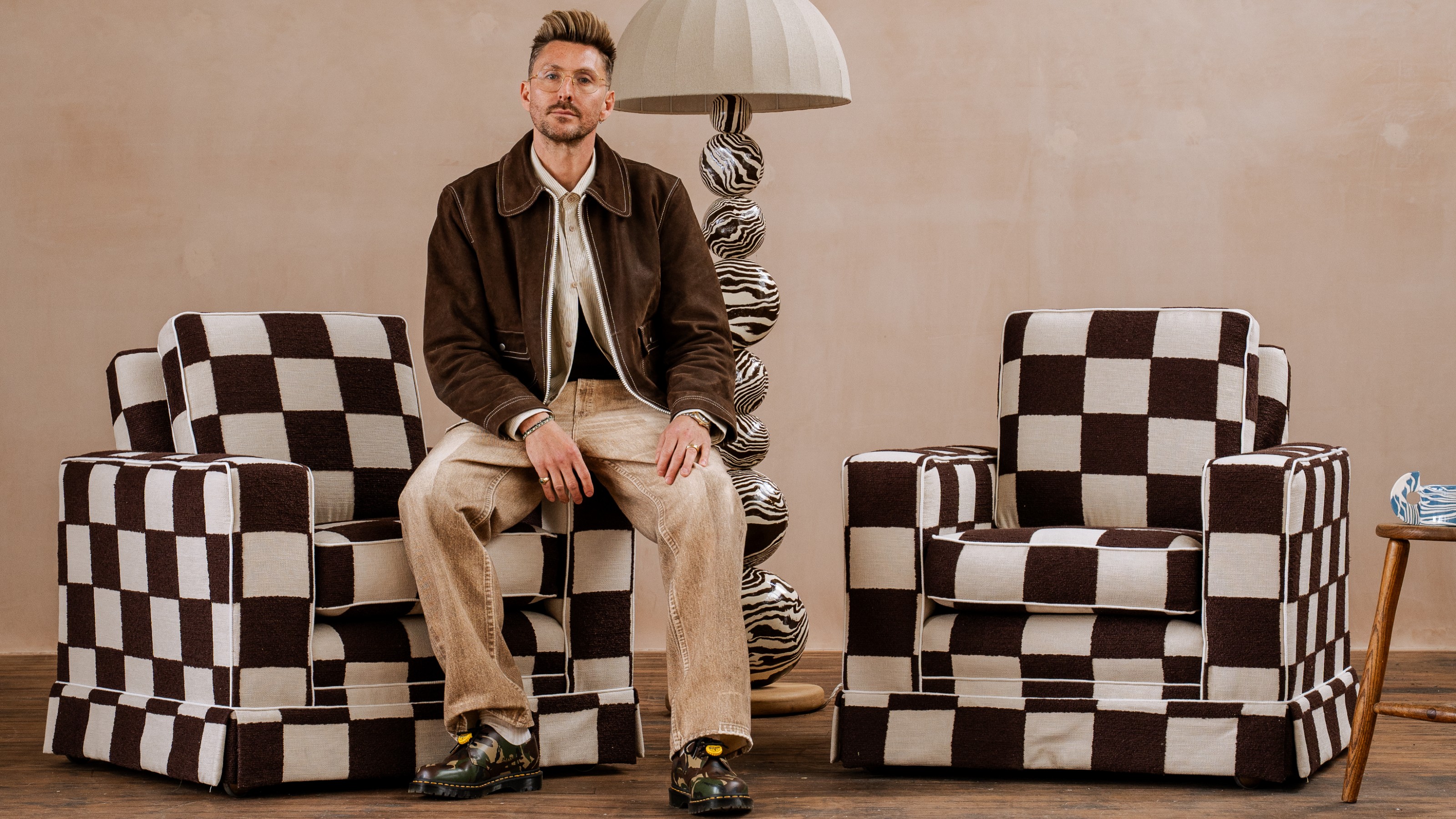 Designer Henry Holland with the Art Deco armchairs reupholstered in the Blenets Check Chocolate fabric from the Harlequin x Henry Holland range