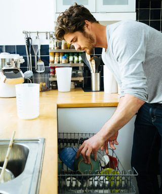 A young man loading a dishwasher in a kitchen