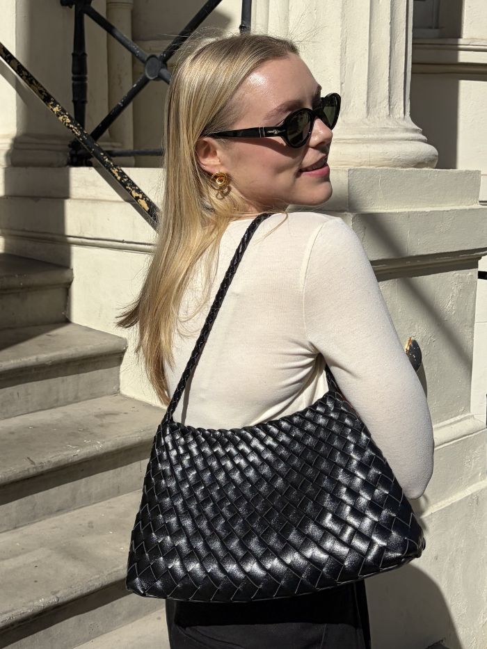 Woman wears white top carries black woven shoulder bag