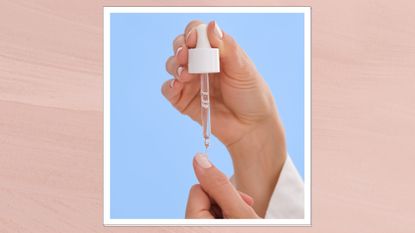 A close up of someone applying a drop of cuticle oil to their pastel pink manicure, against a blue backdrop/ and in a pink template