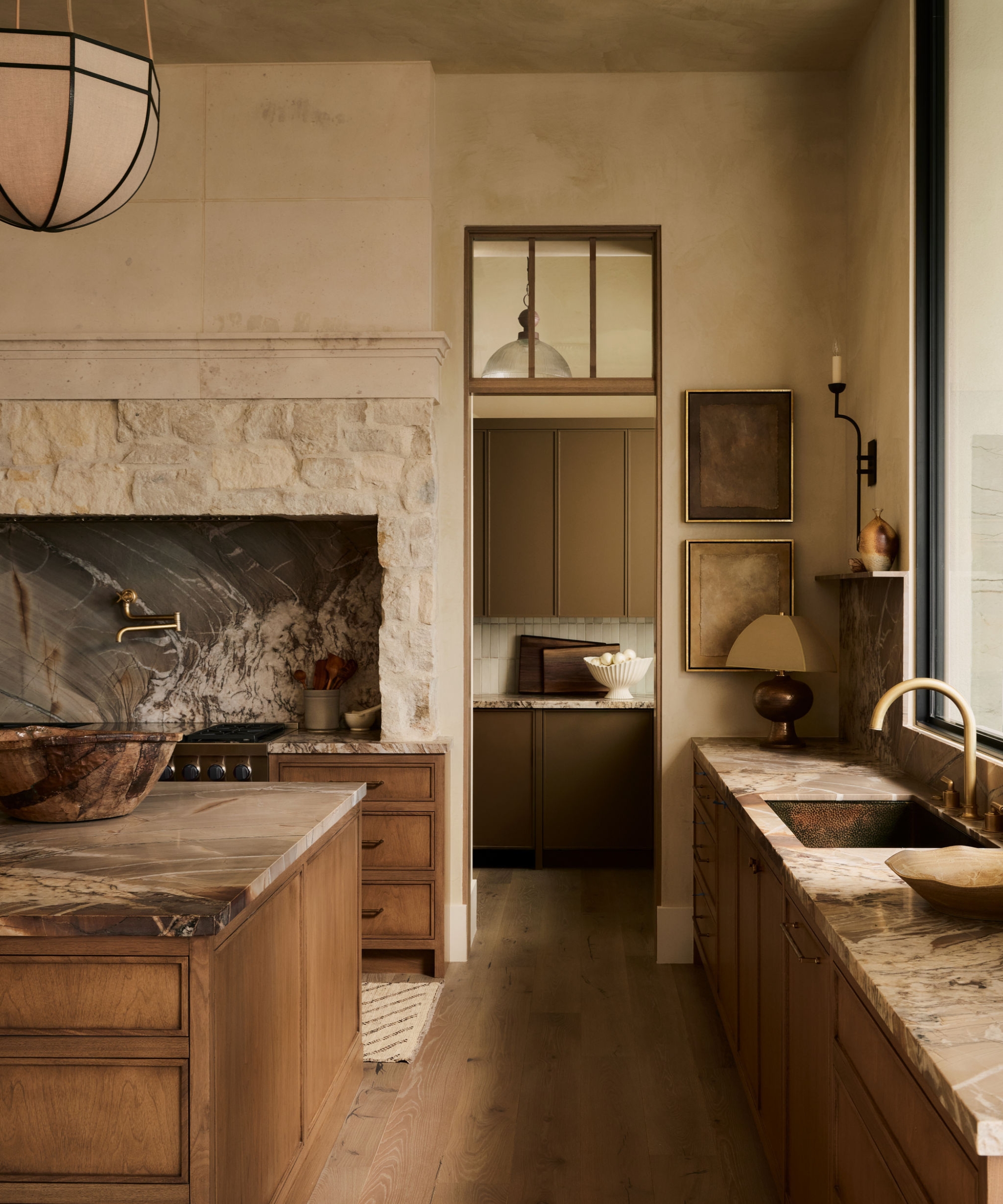 The corner of a neutral kitchen with wood cabinets, stone countertops, limewash walls, and a door into the adjoining pantry