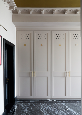 Mudroom with light pink cupboards with brass initials and marble floor