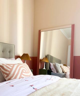 bedroom with dark red lower walls, mirror, peach pink upper walls, gray upholstered bed, blush patterned cushion, cream blanket