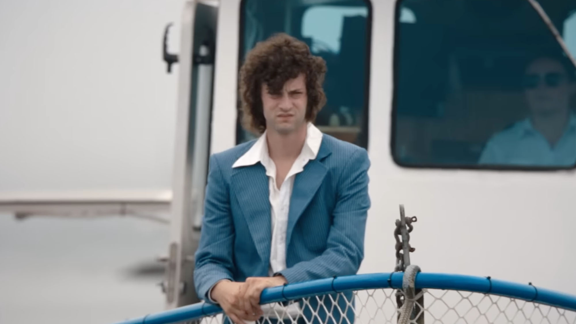 Dominic Sessa in a blue jacket and white shirt, standing on a white boat in Tony