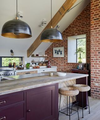 kitchen in room with exposed brick wall, sloped ceiling and kitchen island with dark red doors and large metal pendant lights above