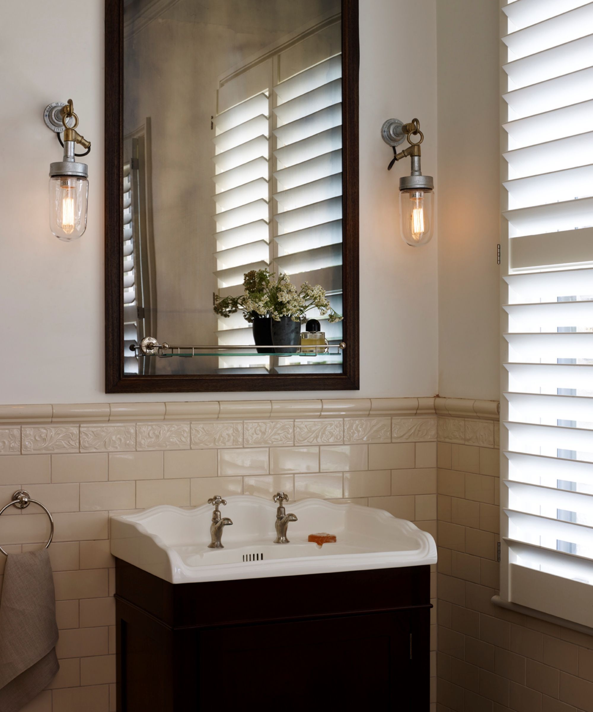 A bathroom basin with a mirror and two industrial style wall lights either side.