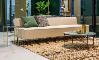 Beige sofa topped with multi-color cushions on a patterned carpet next to a circle shaped coffee table
