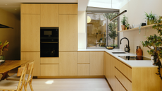 a light-filled kitchen extension with timber kitchen cabinets with no handles and white countertops with a dining table just out of view