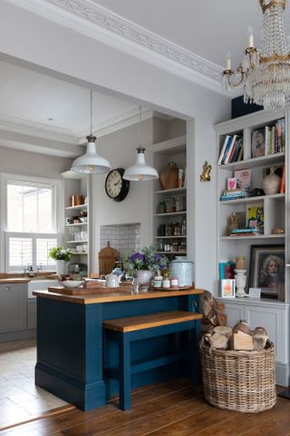 Pippa Jones house: shot towards kitchen with blue painted peninsula and built-in stool, woven basket with logs, and white pendant lights overhead