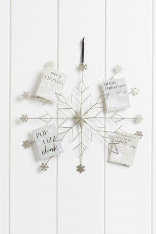A snowflake wire decoration with Christmas card displayed on it with background with white shiplap wall decor