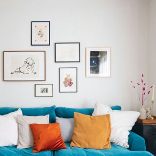 white living room with blue sofa, orange and mustard cushions, gallery wall