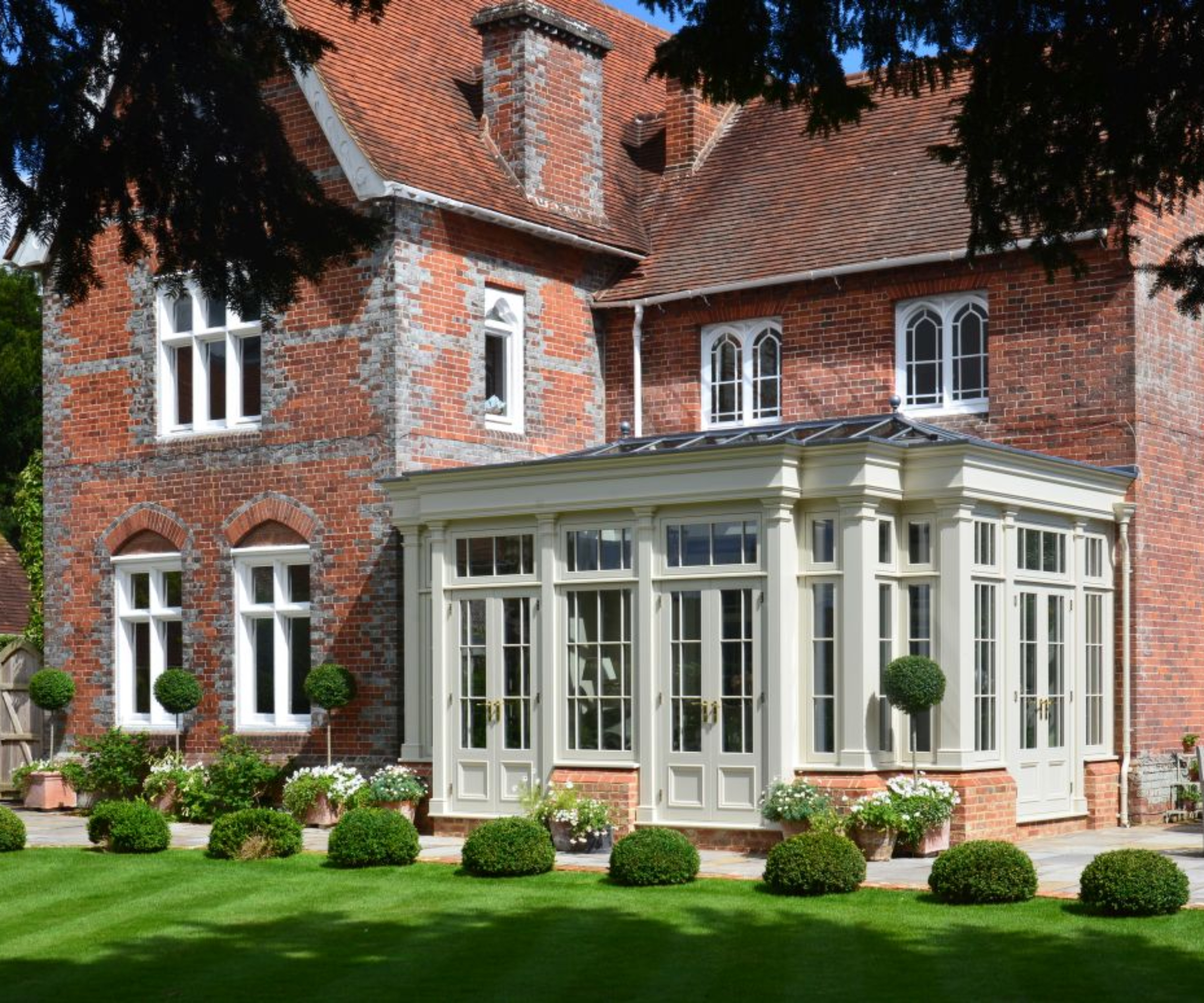 pale green orangery tucked in the return space created by a L-shaped large brick mansion style property