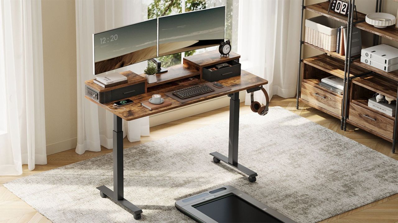 An electric standing desk in rustic brown with two monitors