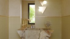yellow bathroom with mosaic tile wall half way with yellow render, stone counter in triangle shape, gold tap, two hand soaps, vase with flowers, and two wall sconces