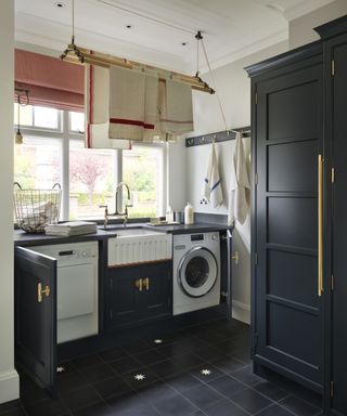 Built-in laundry room storage ideas, including a washing machine, tumble dryer and butler sink, in a black scheme with white walls and gold door handles.