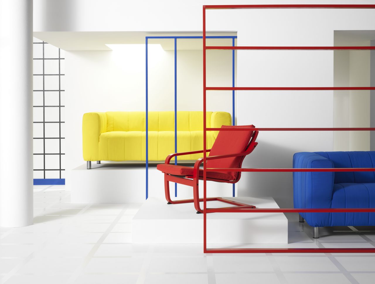 A white room with industrial frames in primary colors and a red POANG recliner chair