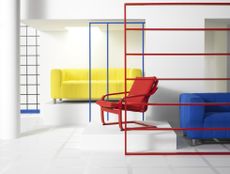 A white room with industrial frames in primary colors and a red POANG recliner chair