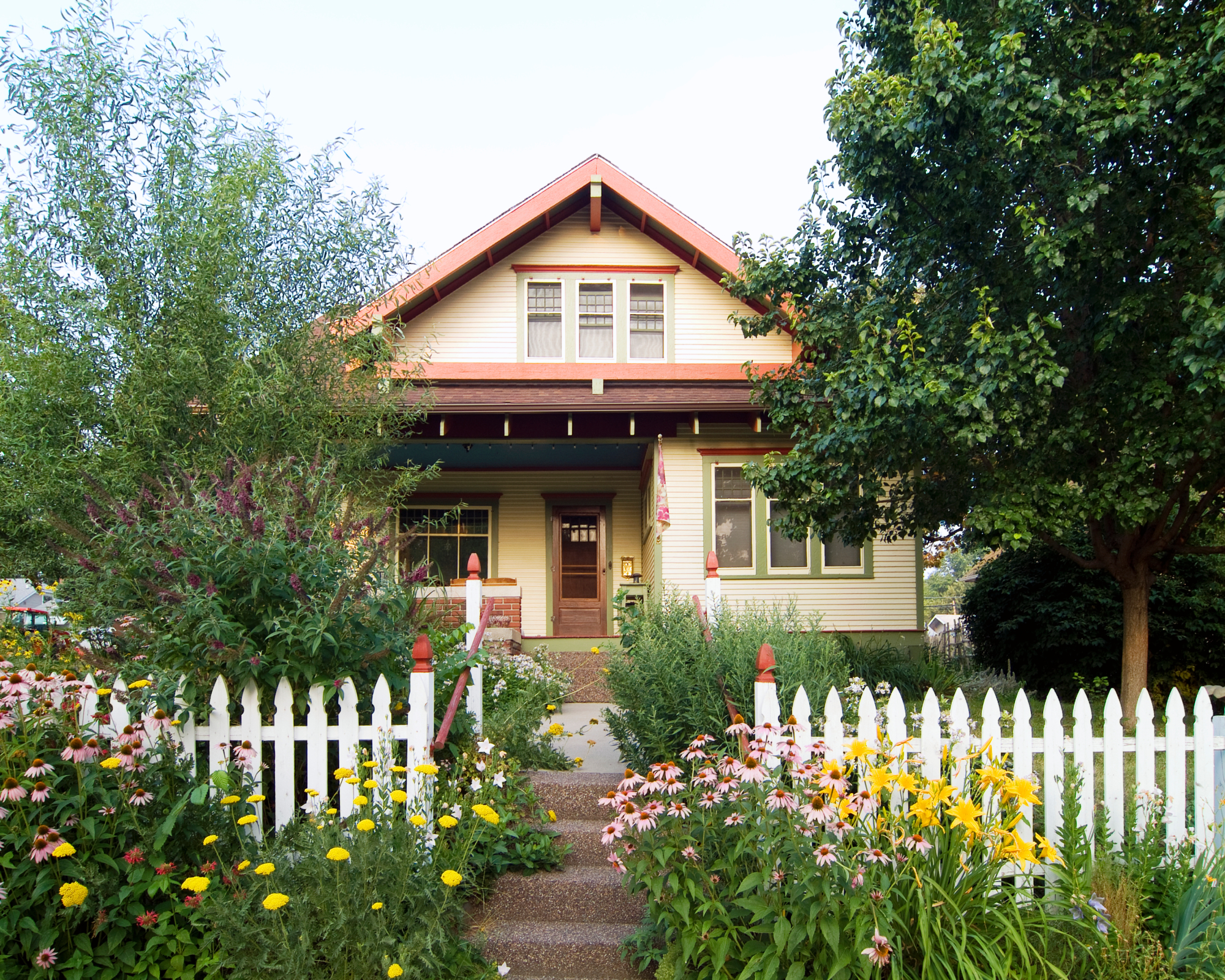 Low-maintenance front yard landscaping with white picket fence, coneflowers, daylilies, yarrow, butterfly bush, and bee balm