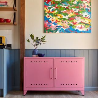 Bisley Fern TV Cabby in Bisley Pink in a wood-panelled kitchen with a vibrant abstract artwork hung above it