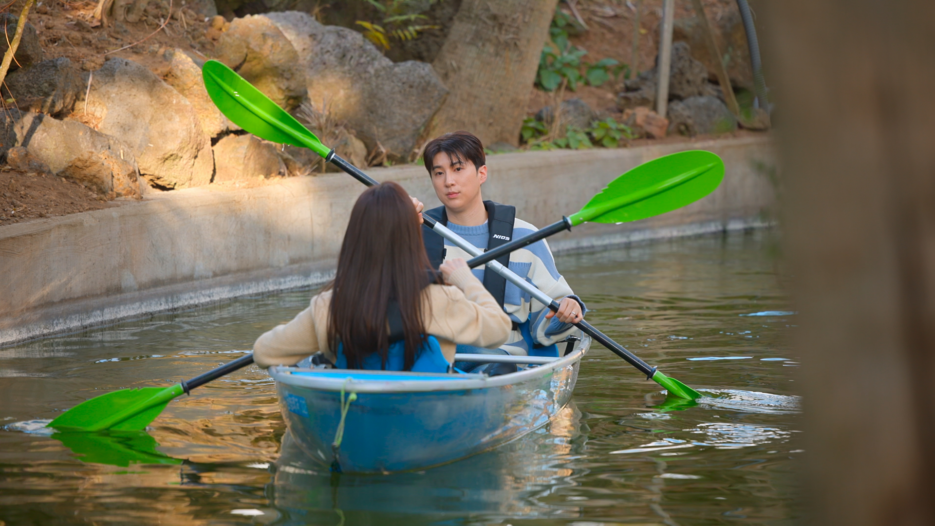 A man and woman use neon green oars to row a blue kayak on a lake, in Netflix's 'Better Late Than Single.'