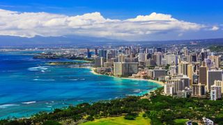 An aerial photo of Honolulu showing the city skyline and beaches on a partly sunny day