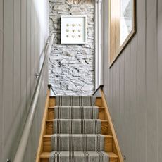 Grey narrow staircase with tongue and groove panelling on either side and exposed stone on the landing wall 