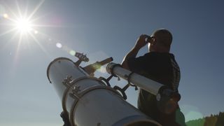 a person looking at the sun while standing next to a telescope