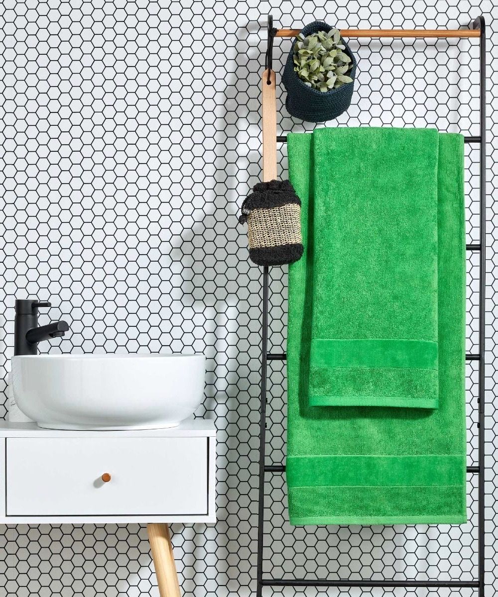 Green towels hanging on towel ladder next to white basin